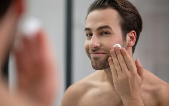 man standing near mirror applying skincare cream to his face